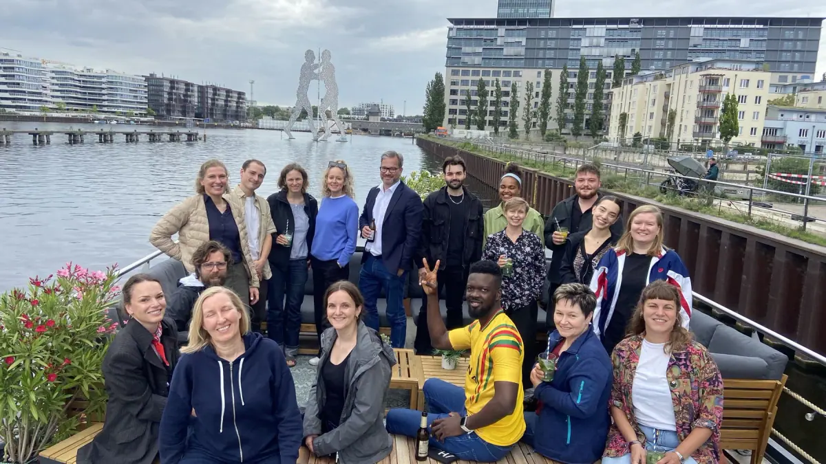 Das Team der IBU Verify GmbH bei einer Floßfahrt auf der Spree vor der Berliner Stadtkulisse